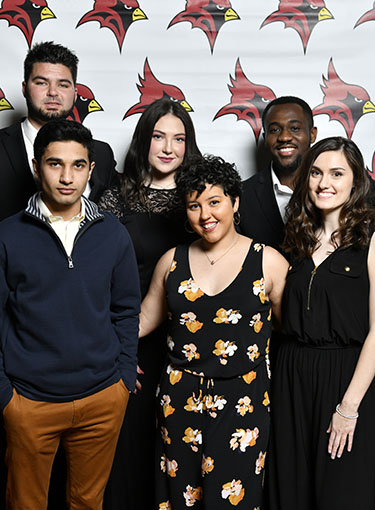 Group of students in front of a cardinal step and repeat background.
