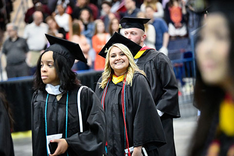 A Fisher student smiles in cap and gown entering the Blue Cross Arena during Commencement.