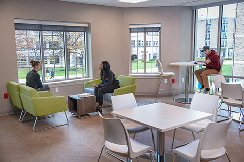 Students sit together at tables and chairs in brightly-lit community space.