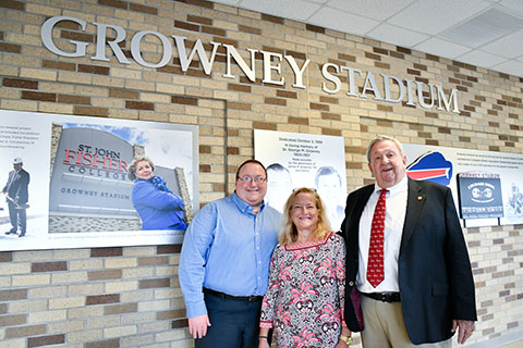Jim Growney, member of the 1948 Society, poses with family members in front of a wall depicting the history of Growney Stadium.
